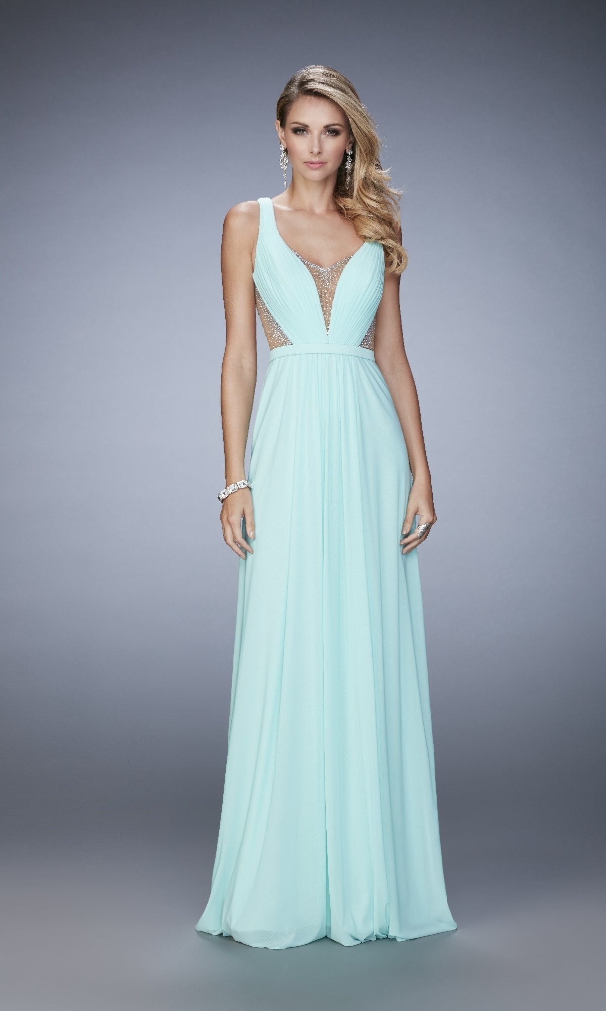 A woman wears the La Femme 22238, a sleeveless light blue A-line long prom dress with a deep V-neckline and mesh side panels, paired with earrings and a bracelet.